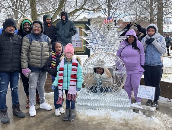 Group of kids and volunteers standing by an ice sculpture at an outing from Camp Phoenix
